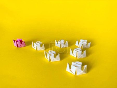 Foto de Grupo de barcos de papel blanco sigue el barco rosa sobre un fondo amarillo. Trabajo en equipo y concepto de liderazgo. Origami - Imagen libre de derechos