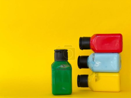 Foto de Cuatro frascos con pintura acrílica multicolor brillante sobre un fondo amarillo. Verde, azul, rojo, amarillo - Imagen libre de derechos
