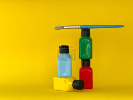 Foto de Cuatro frascos con pintura acrílica de colores brillantes y pincel sobre un fondo amarillo. Verde, azul, rojo, amarillo - Imagen libre de derechos