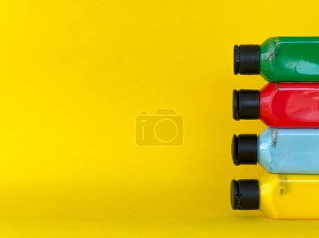 Foto de Cuatro botellas con pintura acrílica multicolor brillante sobre un fondo amarillo. Verde, azul, rojo, amarillo - Imagen libre de derechos