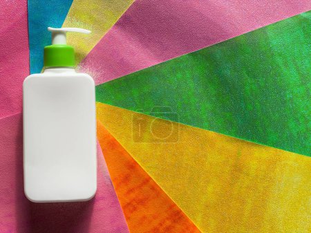 Foto de Botella cosmética plana blanca con dispensador se encuentra en rayas de colores. - Imagen libre de derechos