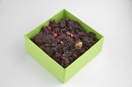 Foto de Hibisco egipcio seco té rojo (karkade) en una caja verde sobre un fondo blanco, primer plano, macro, vista lateral - Imagen libre de derechos