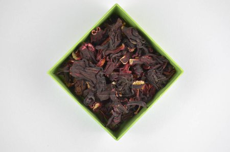 Foto de Hibisco egipcio seco té rojo (karkade) en una caja verde sobre un fondo blanco, primer plano, macro, vista superior - Imagen libre de derechos