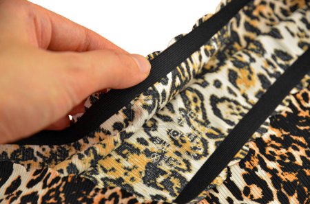 Ropa interior femenina sin costuras (invisible) de leopardo (lencería, bragas, calzoncillos) con borde ondulado aislado primer plano en una mano con una etiqueta impresa en el interior