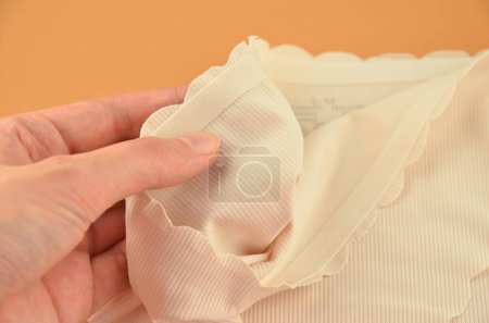 Ropa interior femenina sin costuras (invisible) beige (lencería, bragas, calzoncillos) con borde ondulado aislado, primer plano de goma en una mano
