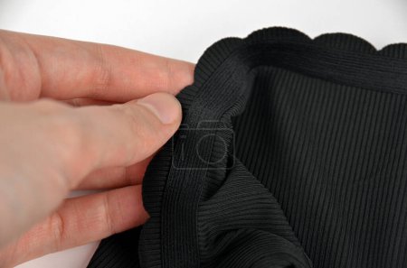Ropa interior femenina inconsútil (invisible) negra (lencería, bragas, calzoncillos) con borde ondulado aislado, primer plano de goma en una mano