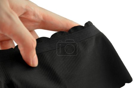 Ropa interior femenina inconsútil (invisible) negra (lencería, bragas, calzoncillos) con borde ondulado aislado, primer plano de goma en una mano