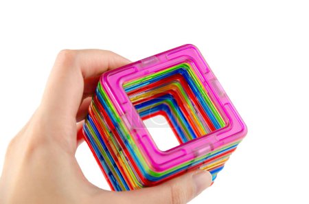Foto de Un grupo de coloridos cuadrados de imanes transparentes (juego de puzzle para niños) conectados en un túnel en una mano sobre un fondo blanco - Imagen libre de derechos