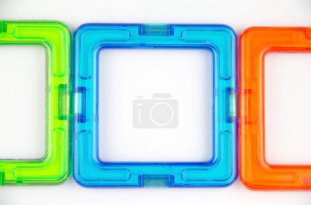 A group of 3 colorful transparent magnet squares (constructor for kids), green, blue and orange in a row, closeup on a white background