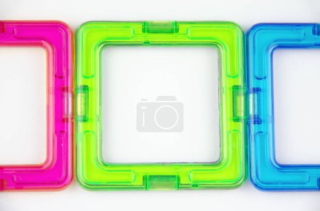 A group of 3 colorful transparent magnet squares (constructor for kids), green, blue and pink in a row, closeup on a white background
