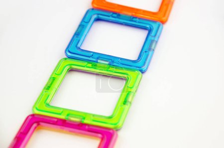 A group of 4 colorful transparent magnet squares (constructor for kids), green, blue, orange and pink in a row, closeup on a white background