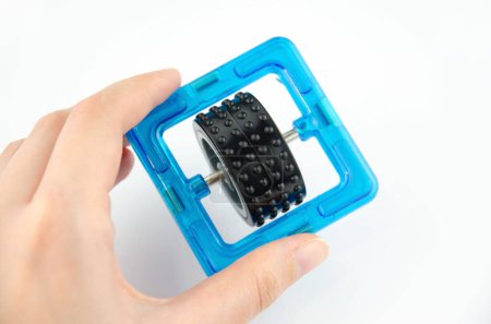 Blue transparent magnet square with black wheel inside (constructor for kids), closeup in a hand on a white background