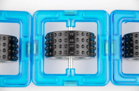 Three blue transparent magnet squares with black wheels inside (constructor for kids), closeup on a white background