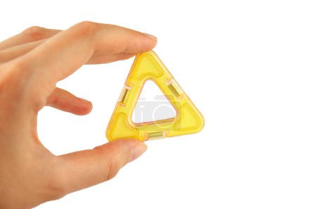 Yellow plastic triangle from transparent magnet constructor kit (puzzle builder for kids) in a hand isolated on a white background