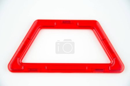 Red plastic trapezoid from transparent magnet constructor kit (puzzle builder for kids) isolated on a white background
