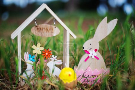 Téléchargez les photos : Maison en bois de Pâques avec lapins, lapin en bois en coquille d'oeuf rose et bougie d'oeuf parmi l'herbe. Concept de Pâques - en image libre de droit