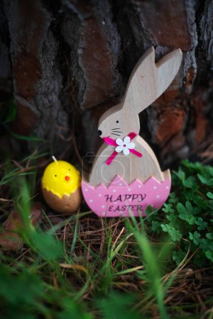 Foto de Conejo de Pascua en cáscara de huevo rosa y vela de huevo entre hierba y con madera sobre fondo. Concepto Pascua - Imagen libre de derechos