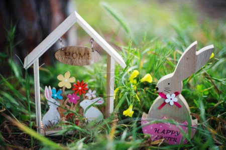 Foto de Conejo de madera de Pascua en cáscara de huevo y casa de madera con conejos entre hierba y flores de primavera. Concepto Pascua - Imagen libre de derechos