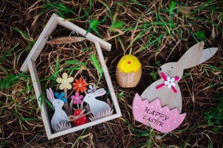 Foto de Casa de madera de Pascua con conejos, conejo en cáscara de huevo rosa y vela de huevo amarillo que yace en la hierba. Concepto Pascua - Imagen libre de derechos
