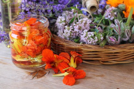 Orange nasturtium flower pickled in alcohol and herbs in a wicker basket.
