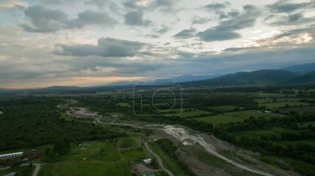 Téléchargez les photos : Paysage rural. Vue aérienne de la campagne. La rivière qui traverse les champs de plantation, la forêt et les montagnes au coucher du soleil. - en image libre de droit