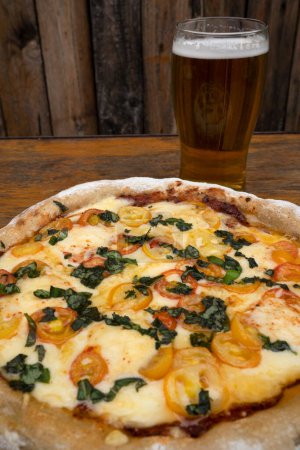 Téléchargez les photos : Pizza avec mozzarella et provolone, ail et tomates cerises et un verre de bière. - en image libre de droit