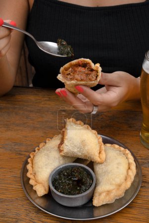 Photo for Eating empanadas at the restaurant. Closeup view of a caucasian woman having fried meat empanadas with traditional chimichurri sauce. - Royalty Free Image