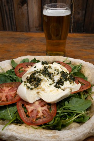 Photo for Pizza and beer. Closeup view of a pizza with burrata cheese, pesto, tomatoes and arugula. - Royalty Free Image