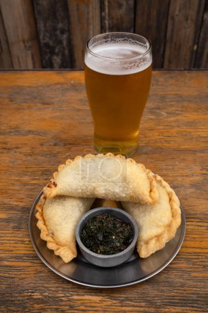 Photo for Closeup view of meat empanadas with spicy chimichurri sauce and a glass of beer. - Royalty Free Image