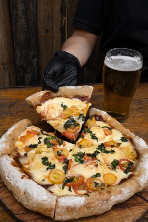 Téléchargez les photos : Vue rapprochée d'un chef portant des gants, présentant une tranche de pizza avec mozzarella et provolone fromage, ail et tomates cerises. - en image libre de droit