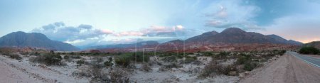 Photo for The desert at sunset. Panorama view of the desert flora, colorful mountains, sand, rock formations and asphalt highway across the arid valley under a beautiful sky with dusk colors. - Royalty Free Image