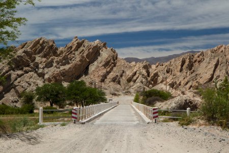 Téléchargez les photos : Voyager le long de la route de terre à travers le désert aride. Vue sur la route et le pont sur la rivière. Le grès et les formations rocheuses en arrière-plan. - en image libre de droit