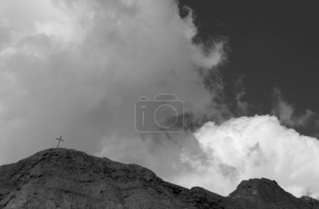 Foto de Paisaje blanco y negro. Religión. Cruz de acebo en la cima de la montaña, bajo un cielo dramático con hermosas nubes. - Imagen libre de derechos
