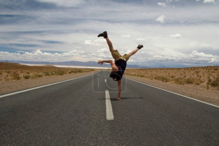 Téléchargez les photos : Breakdance. Loisirs. Jeune homme caucasien handstand et tourbillon dans la route du désert d'asphalte. - en image libre de droit