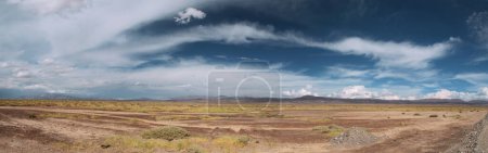 Photo for Panorama view of the arid desert, valley, grass and mountains in the background under a beautiful blue sky with dramatic clouds. - Royalty Free Image