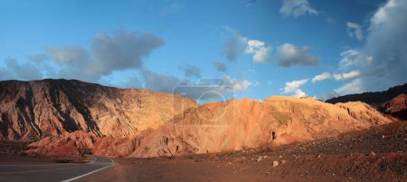 Photo for The asphalt highway across the desert at sunset. Beautiful panorama view of the empty road along the arid valley, the red sand, sandstone and rocky hills with a dusk light. - Royalty Free Image
