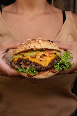 Téléchargez les photos : Burger géant. Vue rapprochée d'un délicieux hamburger au fromage, laitue, tomate, oignon, viande grillée, bacon croustillant et pomme de terre au pain provolone, avec un fond en bois. - en image libre de droit