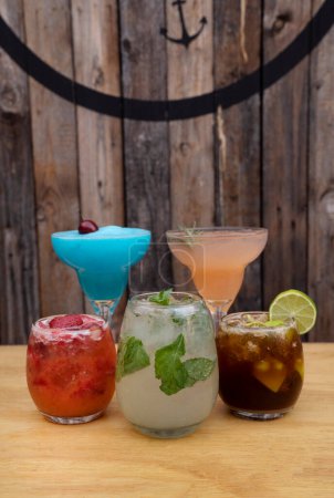 Foto de Hora feliz. Vista de cerca de tres vasos y dos tazas con bebidas tropicales alcohólicas con un fondo de madera. - Imagen libre de derechos
