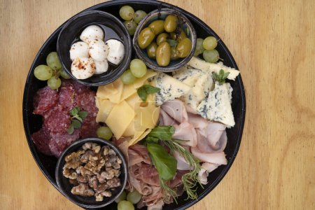 Photo for Food on the restaurant table. Close-up view of different dishes on wooden background. Meal with sliced salami, cheese, blue cheese, focaccia bread, italian boconccinos, walnuts, ham, cured ham and green olives on the wooden table. - Royalty Free Image