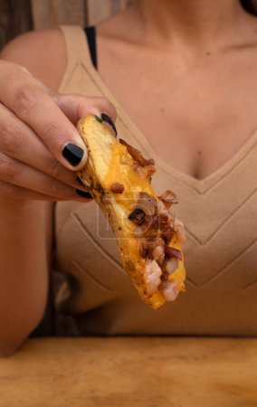 Foto de Comiendo papas fritas en el restaurante. Vista de cerca de la mano de una mujer sosteniendo una papa frita con tocino crujiente y salsa de queso cheddar. - Imagen libre de derechos