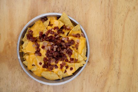 Téléchargez les photos : Nachos avec fond de cheddar. Vue de dessus des nachos au fromage cheddar et du bacon croustillant dans un plat en métal sur la table en bois. - en image libre de droit