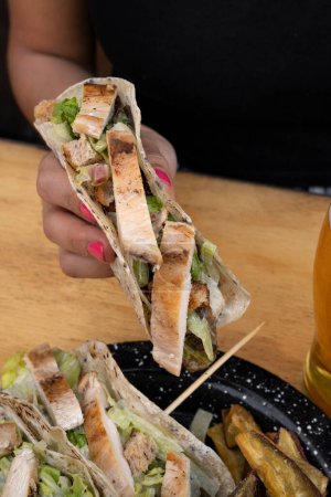 Photo for Having tacos and a pint of beer. Closeup view of a woman holding a taco with grilled chicken breast and lettuce. - Royalty Free Image