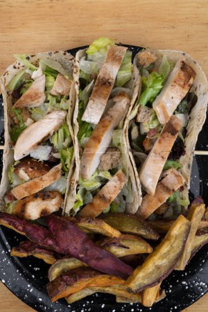 Téléchargez les photos : Gastronomie fusion. Vue du dessus d'un plat noir avec tacos de salade César et patates douces frites sur la table en bois. - en image libre de droit