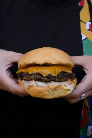 Foto de Mujer sosteniendo una hamburguesa tradicional con queso y cebolla. - Imagen libre de derechos