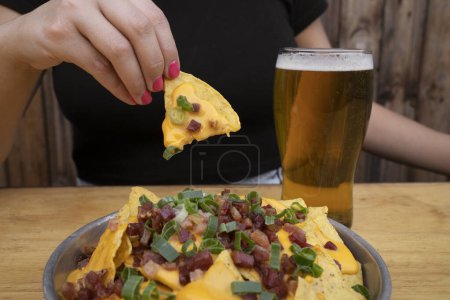 Photo for Eating nachos. Closeup view of a woman holding a nacho with cheddar cheese, green onion and crispy bacon. - Royalty Free Image