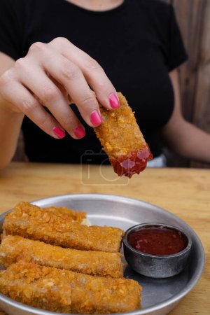 Photo for Gastronomy. Closeup view of woman's holding a fried mozzarella cheese stick dipped in a spicy sauce. - Royalty Free Image