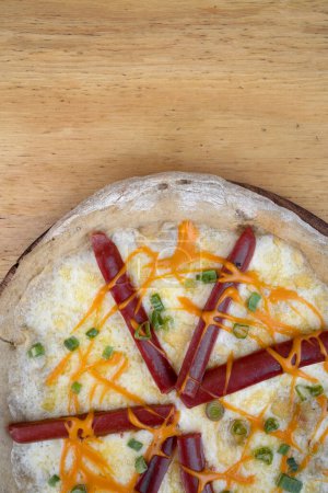 Foto de Pizza. Vista superior de la pizza de queso mozzarella con queso cheddar, cebolla verde y salchichas ahumadas, en la mesa de madera. - Imagen libre de derechos