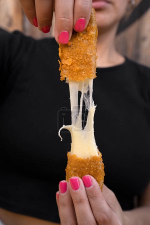 Photo for Woman stretching fried mozzarella cheese sticks. - Royalty Free Image