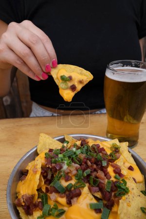 Téléchargez les photos : Manger des nachos. Vue rapprochée d'une femme tenant un nacho au fromage cheddar, oignon vert et bacon croustillant. - en image libre de droit