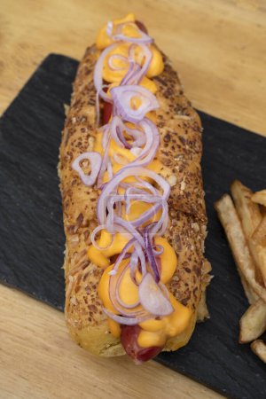 Téléchargez les photos : Hot dog à l'oignon rouge, fromage cheddar et frites dans un plat noir. - en image libre de droit